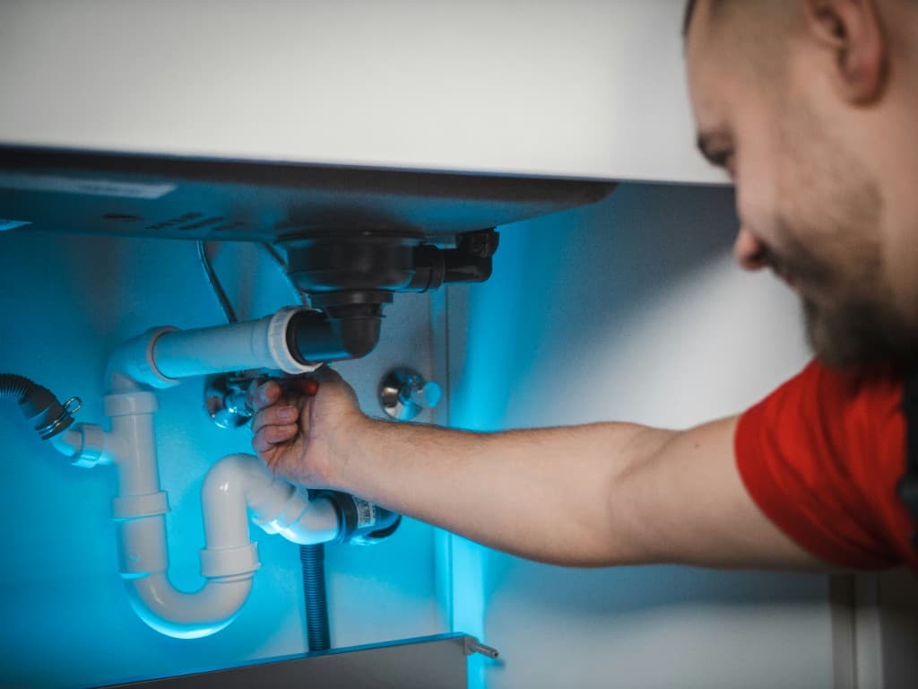Plumber repairing pipes under a kitchen sink